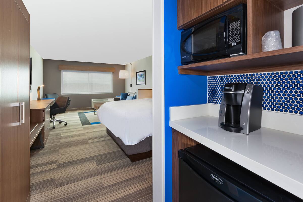 Een hotelkamer met een bed, bureau, stoel, kitchenette en een raam met zonwering.