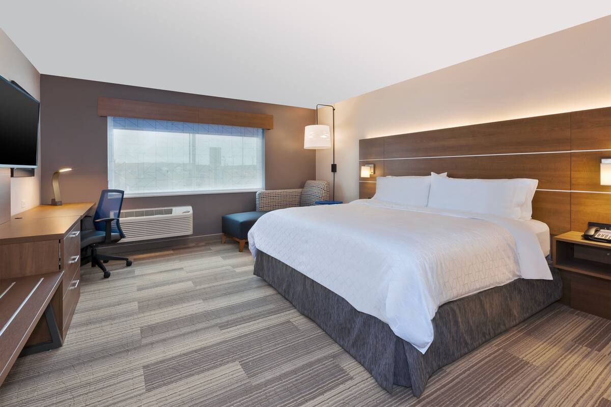 Een moderne hotelkamer met een groot bed, een bureau, een stoel, een televisie en een raam met luxaflex.