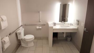 A modern bathroom with a toilet, handrail, sink, mirror, and a trash bin.