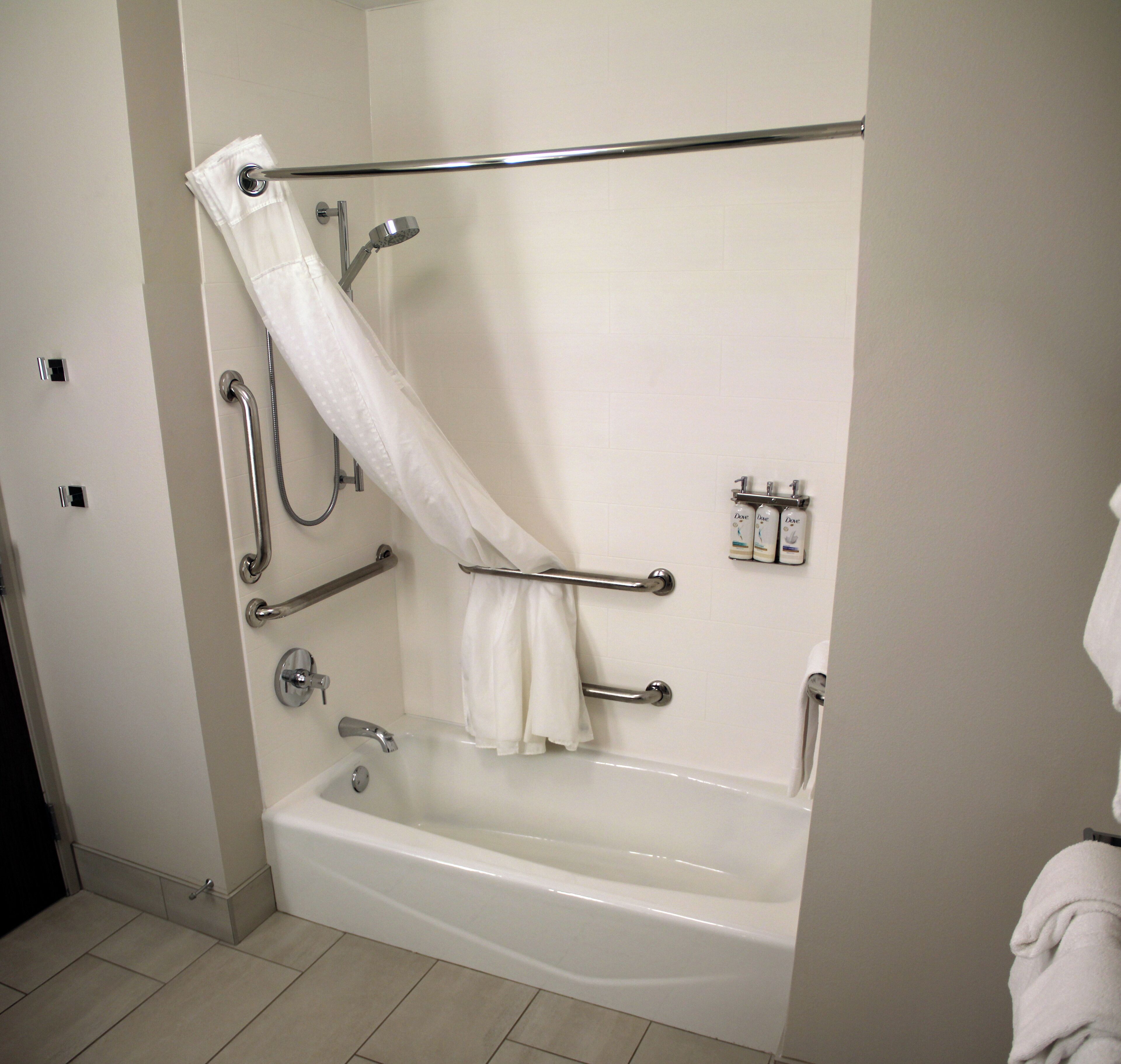 A standard bathroom with a bathtub, grab bars, a shower head, and a hand-held shower attachment.