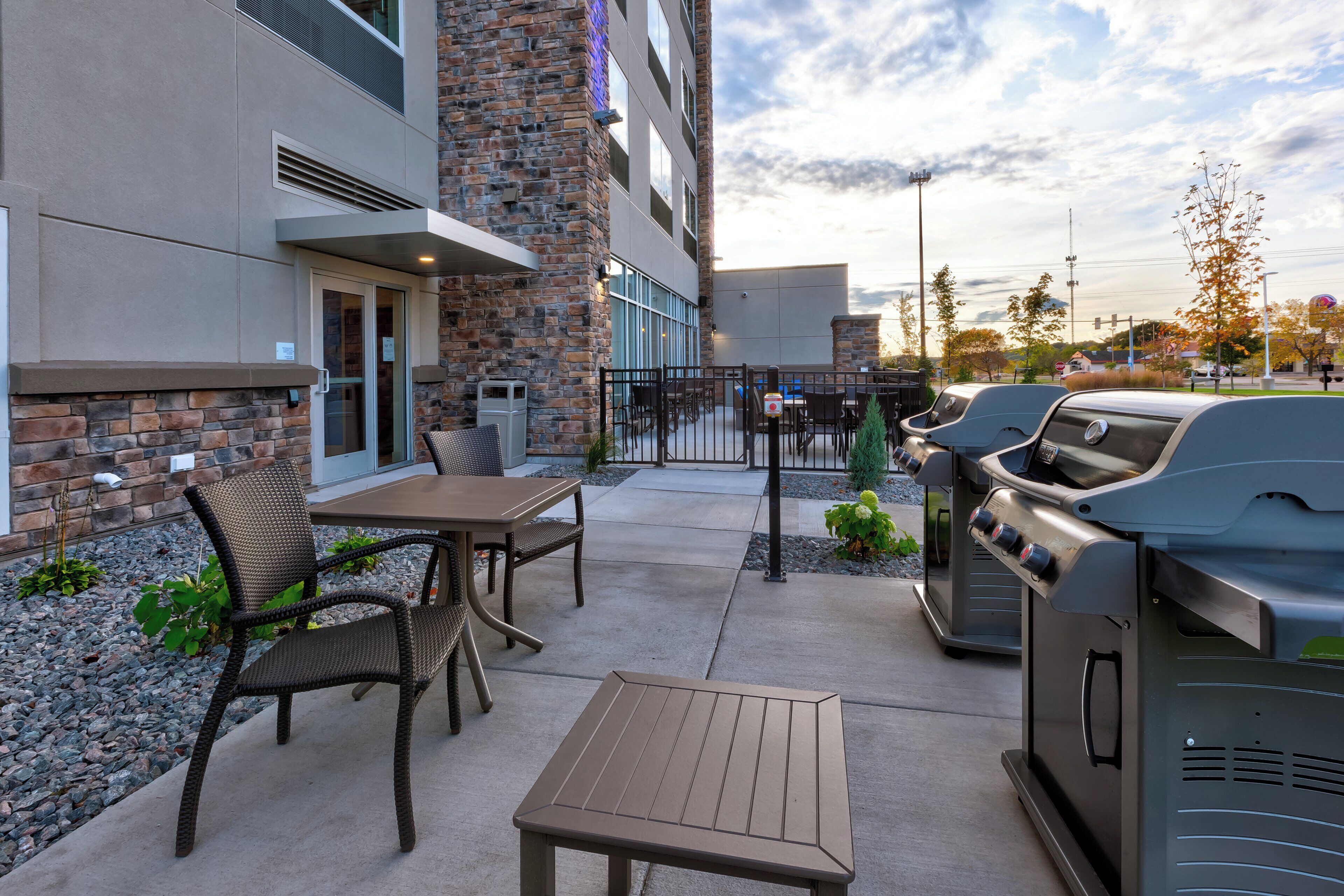 Un patio exterior con una parrilla, un área de estar y un edificio de fachada de piedra y ladrillo.