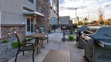 Un patio exterior con una parrilla, un área de estar y un edificio de fachada de piedra y ladrillo.