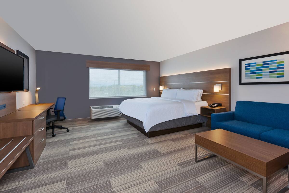 Een hotelkamer met een bed, een bureau, een stoel, een bank, een televisie en een raam.
