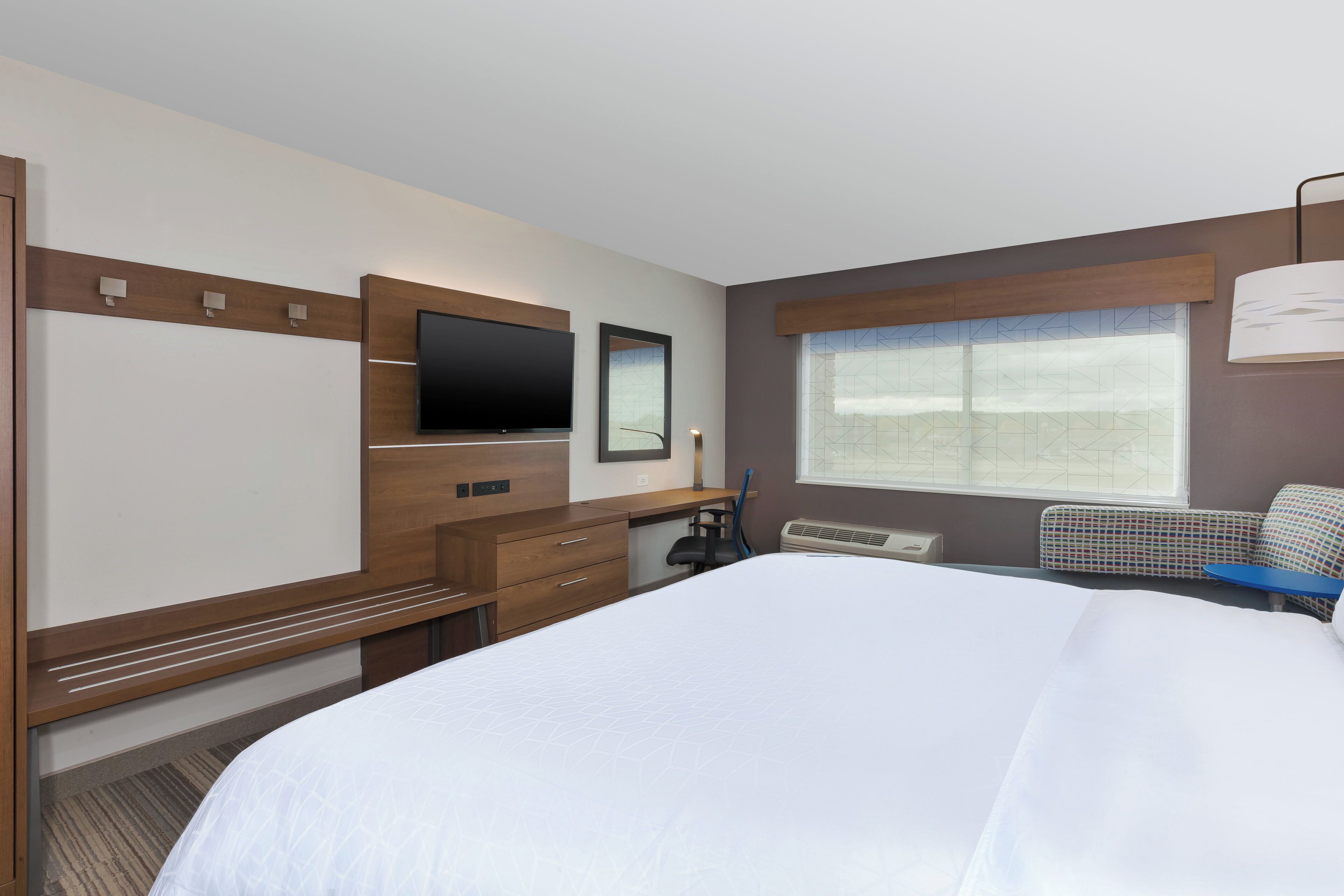 Una habitación de hotel con cama, escritorio, silla, televisor y ventana.