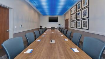 A conference room with a long table, blue chairs, a flat-screen TV, and framed artwork on the wall.