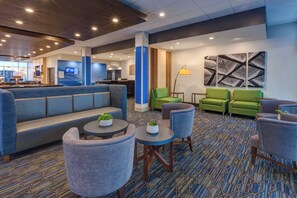 A hotel lobby with a blue sofa, green chairs, a patterned carpet, and a large artwork on the wall.