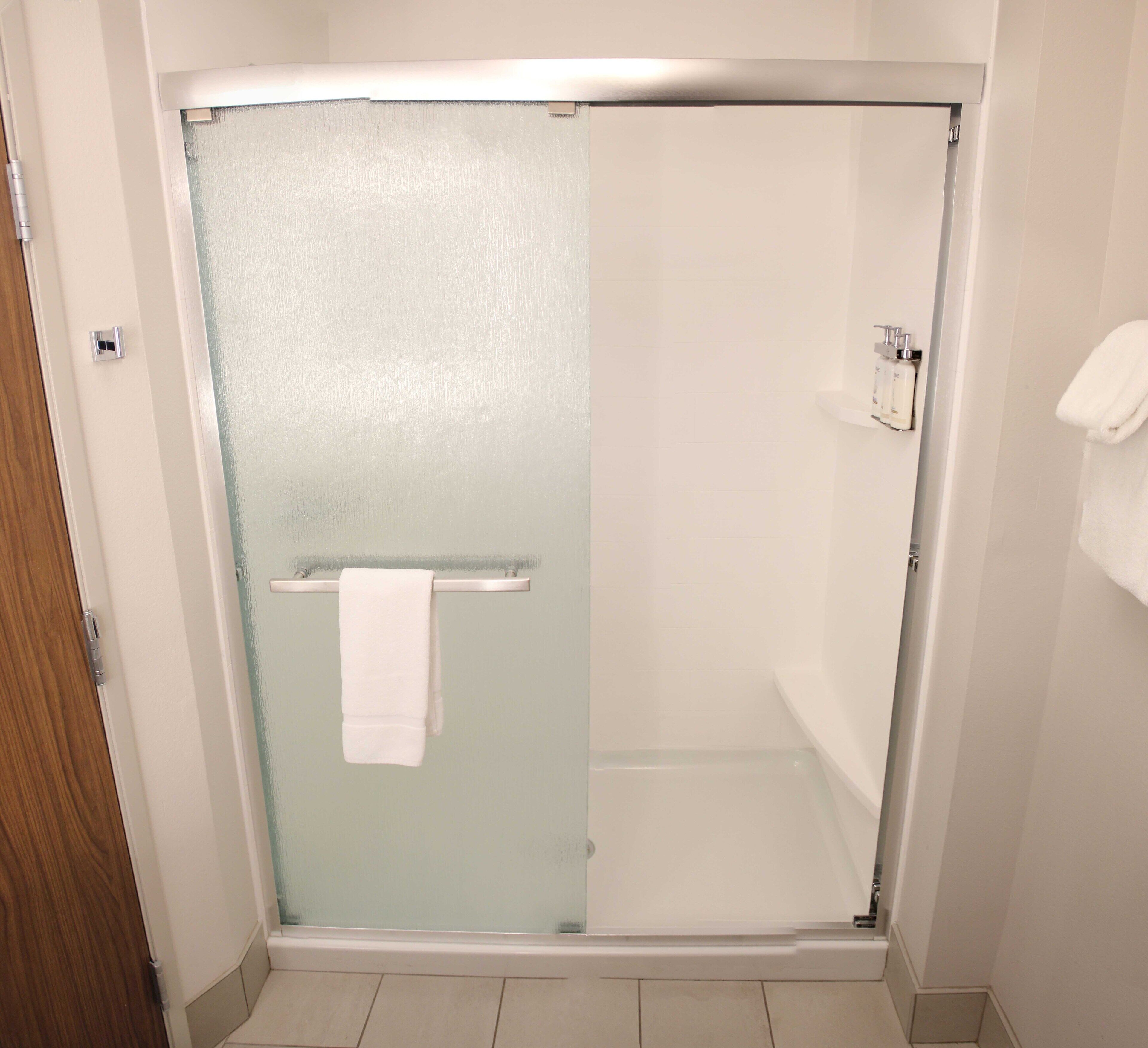 A bathroom with a glass shower enclosure, a white towel hanging on a rack, and a white sink with toiletries.