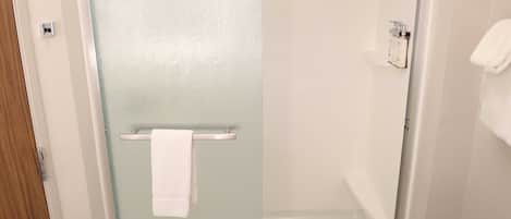 A bathroom with a glass shower enclosure, a white towel hanging on a rack, and a white sink with toiletries.