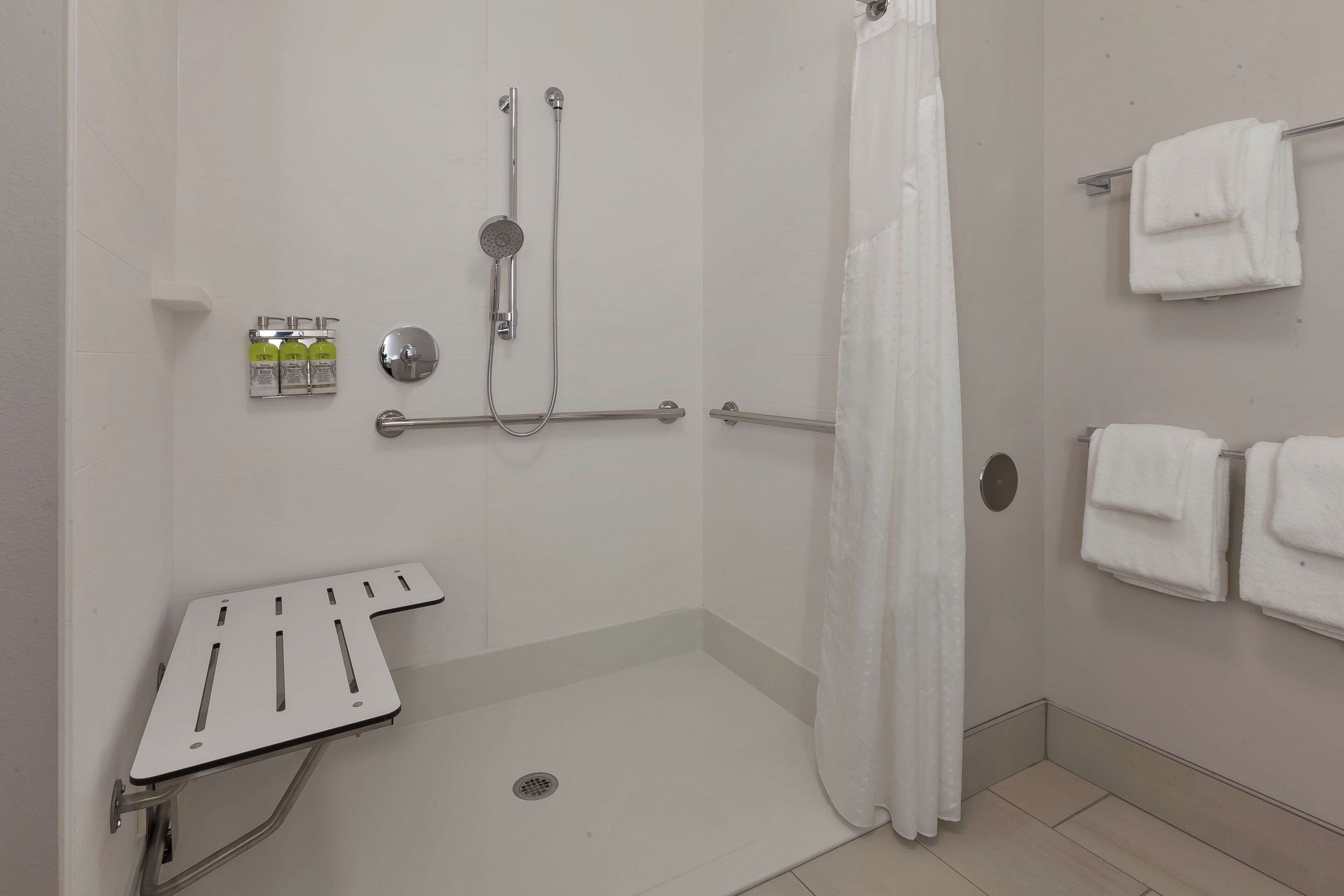 Un baño con ducha, barras de apoyo, inodoro y toallero.