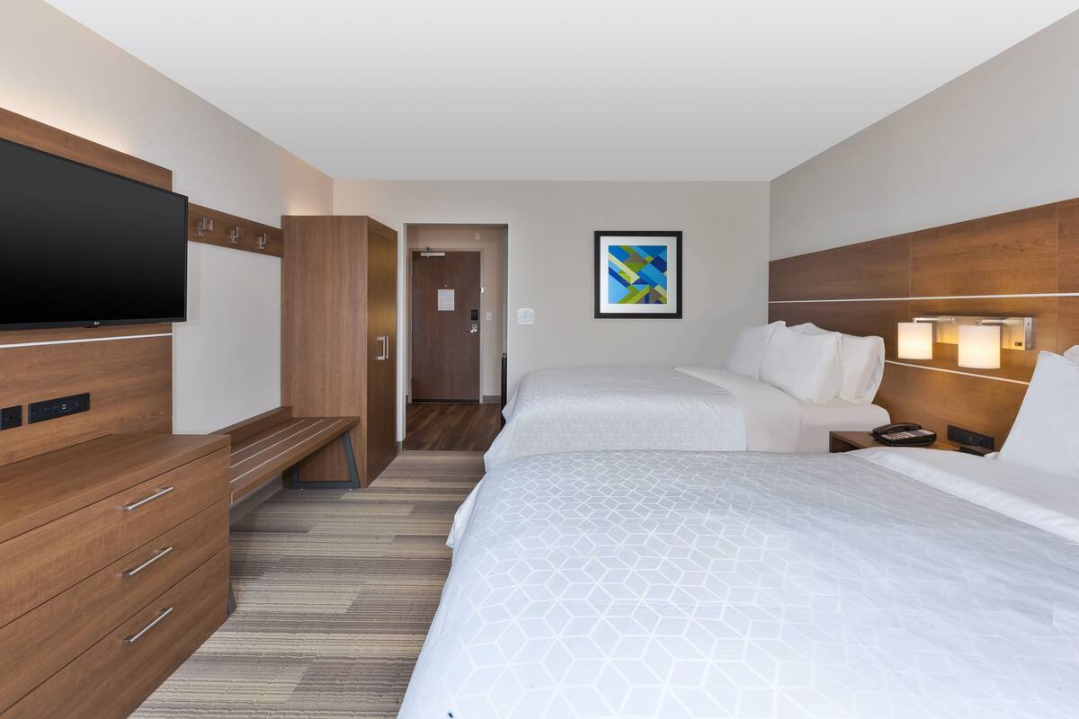 Een hotelkamer met twee bedden, een televisie, houten meubels en een schilderij aan de muur.