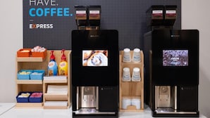 Twee koffieautomaten met digitale displays, een koffieautomaat en een plank met koffiecups en een koffiezetapparaat.