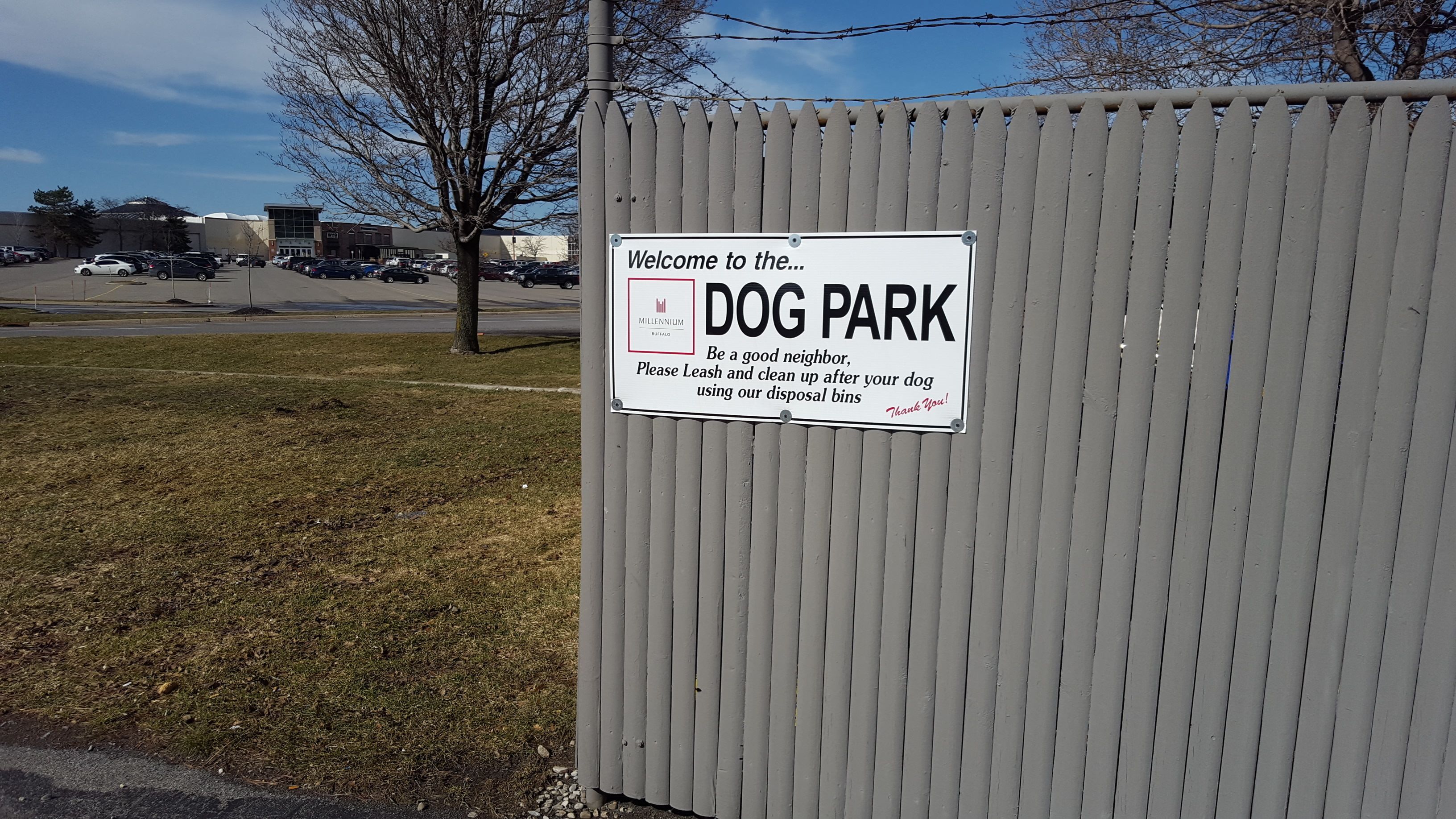 Skilt der byder besøgende velkommen til en hundepark, og som instruerer dem i at holde hunde i snor og rengøre efter dem med affaldsspande.