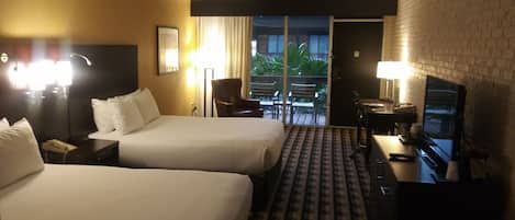 A hotel room with two beds, a desk with a television, and a view of the outdoors.