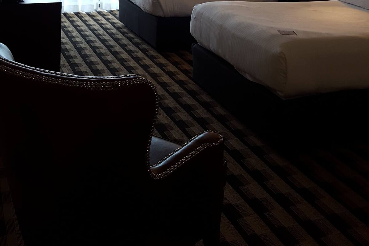 Habitación de hotel con dos camas, un escritorio, una silla y un ventanal con cortinas.