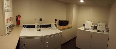 A laundry area with multiple washing machines, a soap and bleach dispenser, and a fire extinguisher.