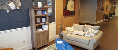 A reception area with a wooden bookshelf, a white sofa, and a blue surfboard.