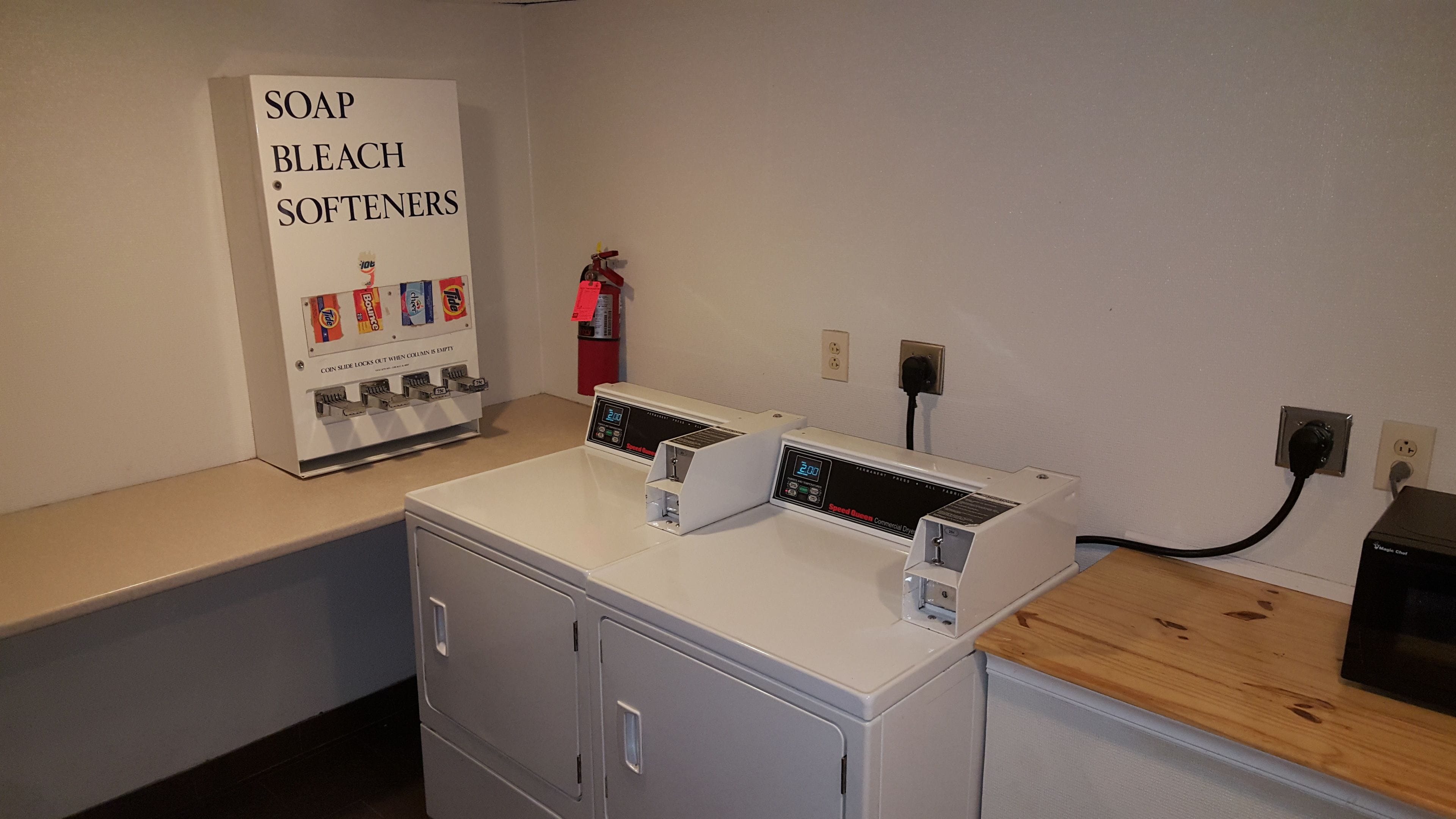 A laundry area with a coin-operated soap, bleach, and softener dispenser, a washing machine, and a dryer.