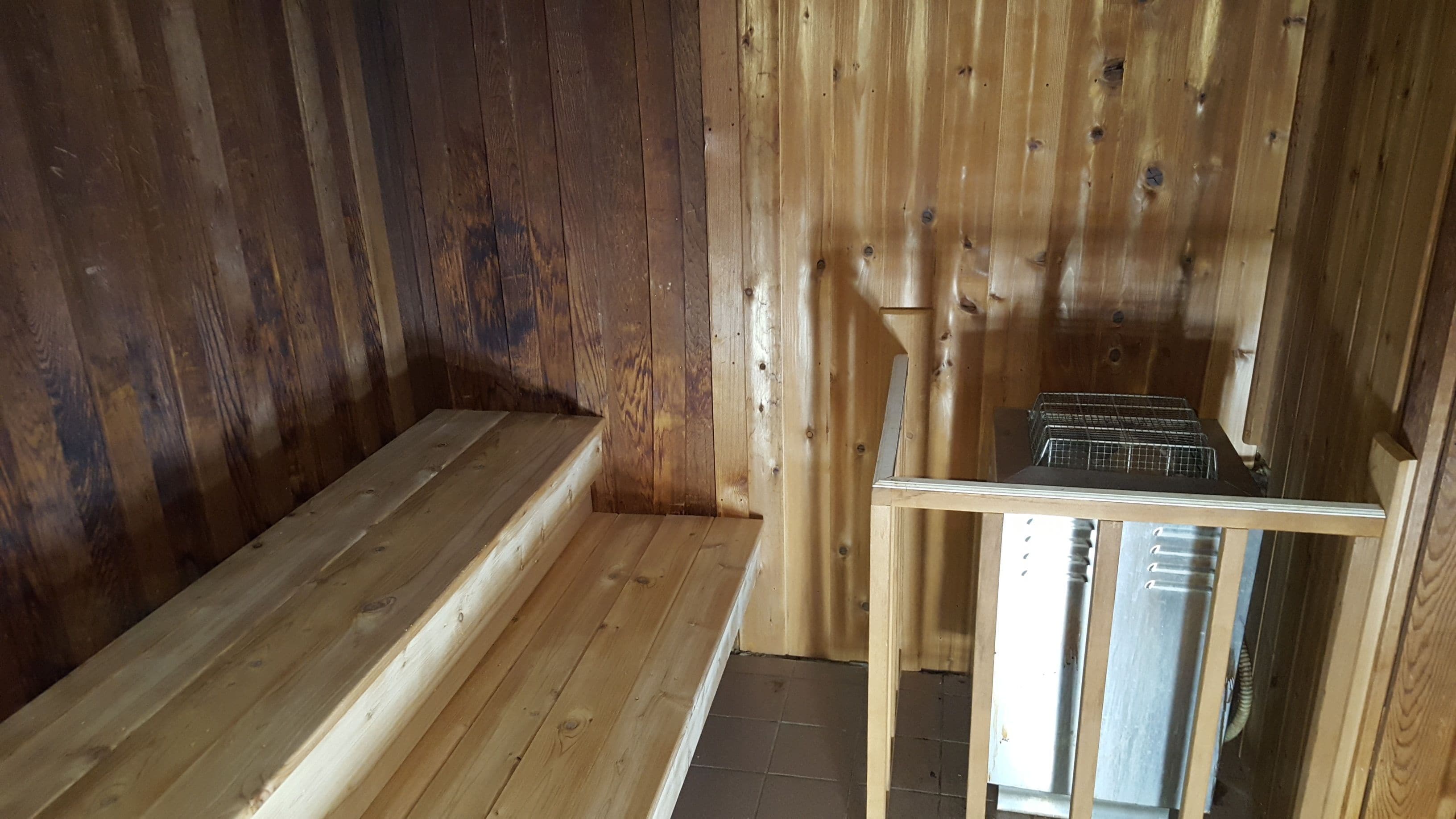 A wooden cabin interior with a bench and a metal rack.