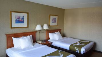 Quarto de hotel com duas camas, uma cabeceira de madeira, mesa de cabeceira com abajur e duas fotos emolduradas na parede.