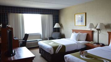 A hotel room with a large bed, a desk with a computer, a chair, and a window with curtains.