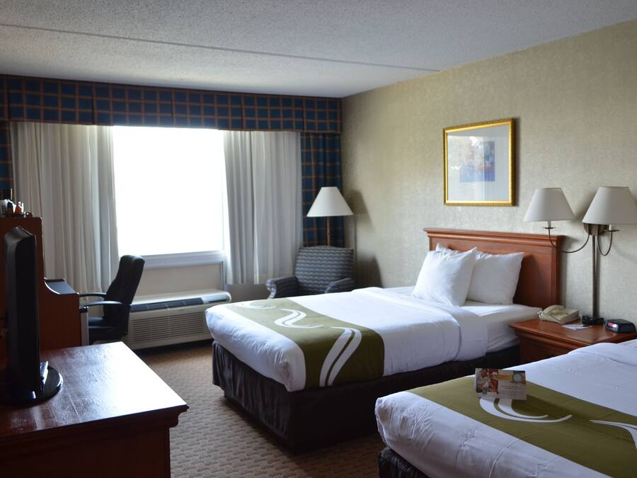 A hotel room with a large bed, a desk with a computer, a chair, and a window with curtains.