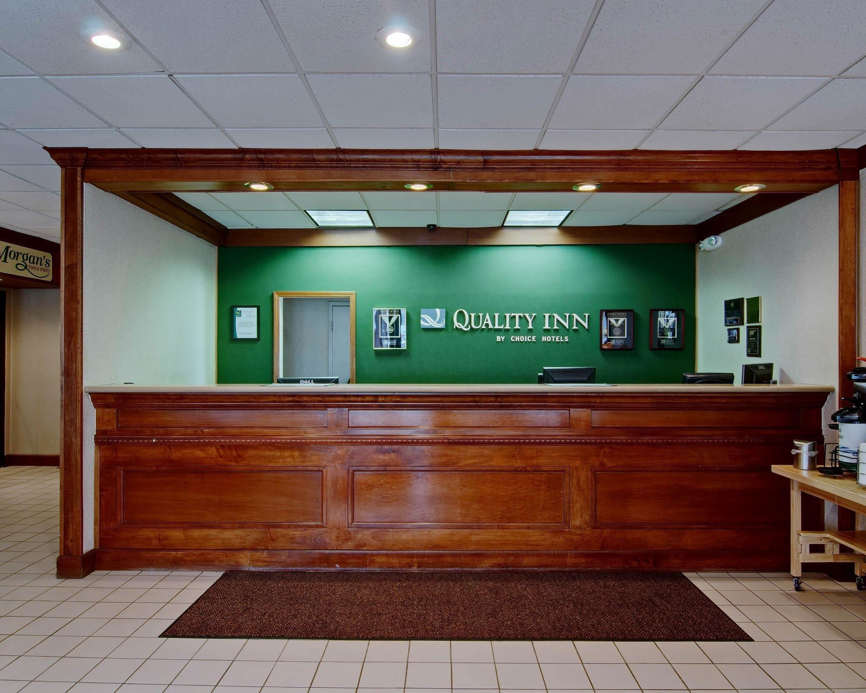 Un comptoir d’accueil avec un mur végétal, une enseigne indiquant « Quality Inn by Choice Hotels » et des trophées encadrés accrochés au mur.