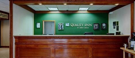 Un comptoir d’accueil avec un mur végétal, une enseigne indiquant « Quality Inn by Choice Hotels » et des trophées encadrés accrochés au mur.