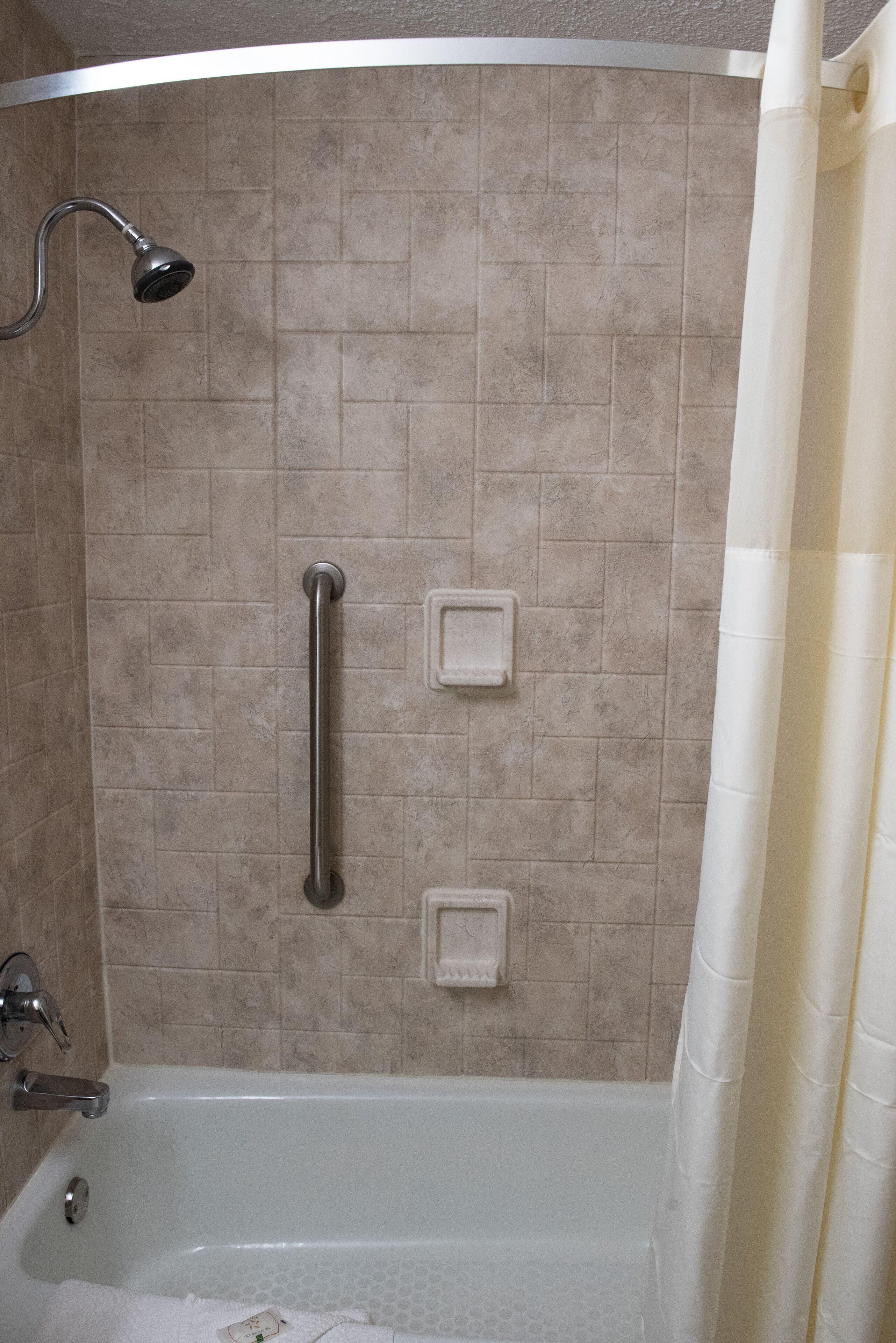 Baño con bañera, ducha y barras de apoyo.