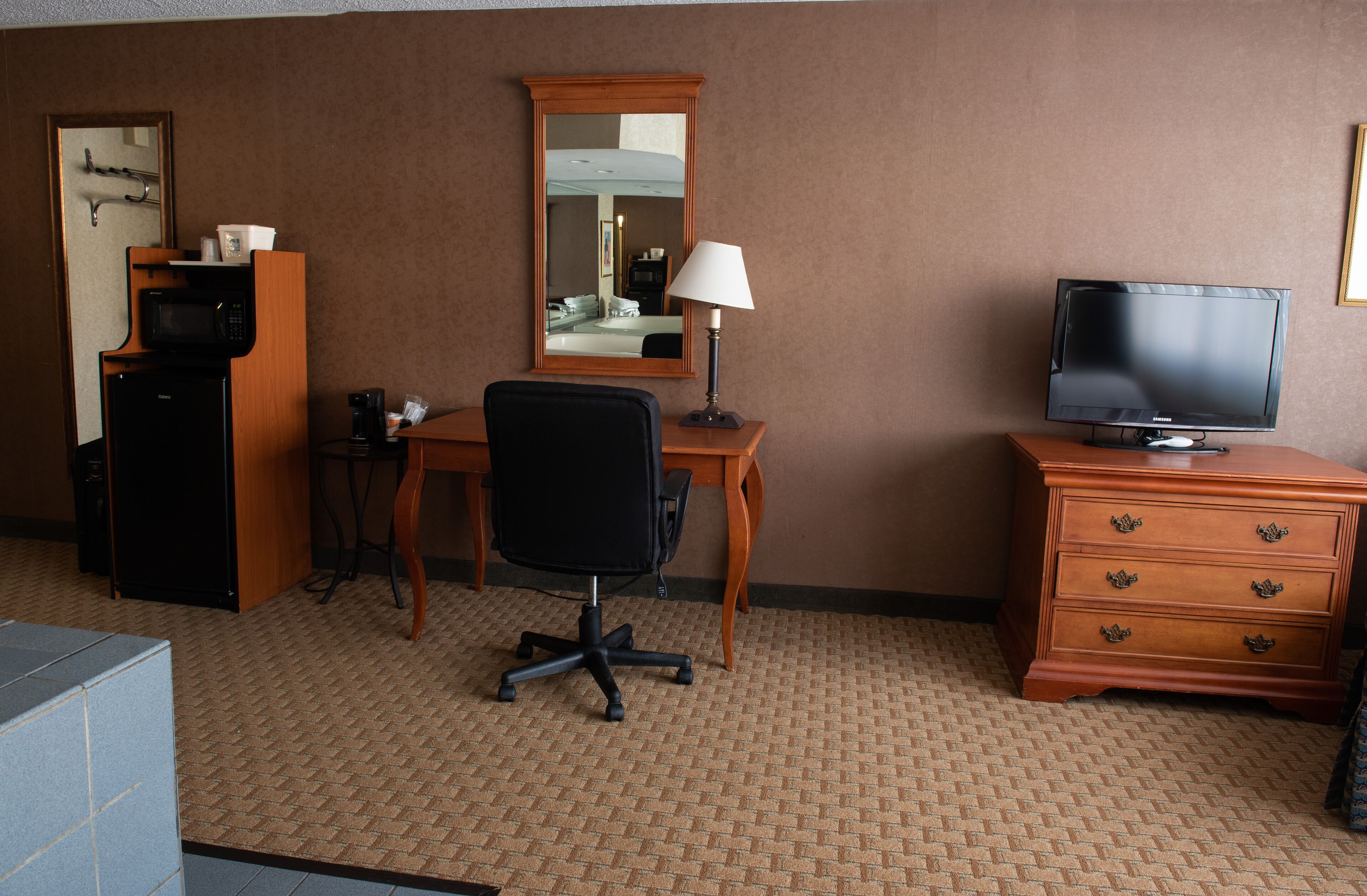 A hotel room with a desk, chair, television, dresser, microwave, and coffee maker.