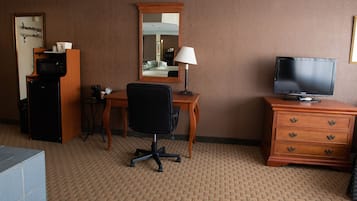 A hotel room with a desk, chair, television, dresser, microwave, and coffee maker.