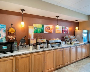 A breakfast bar with various food items, a microwave, and a refrigerator.