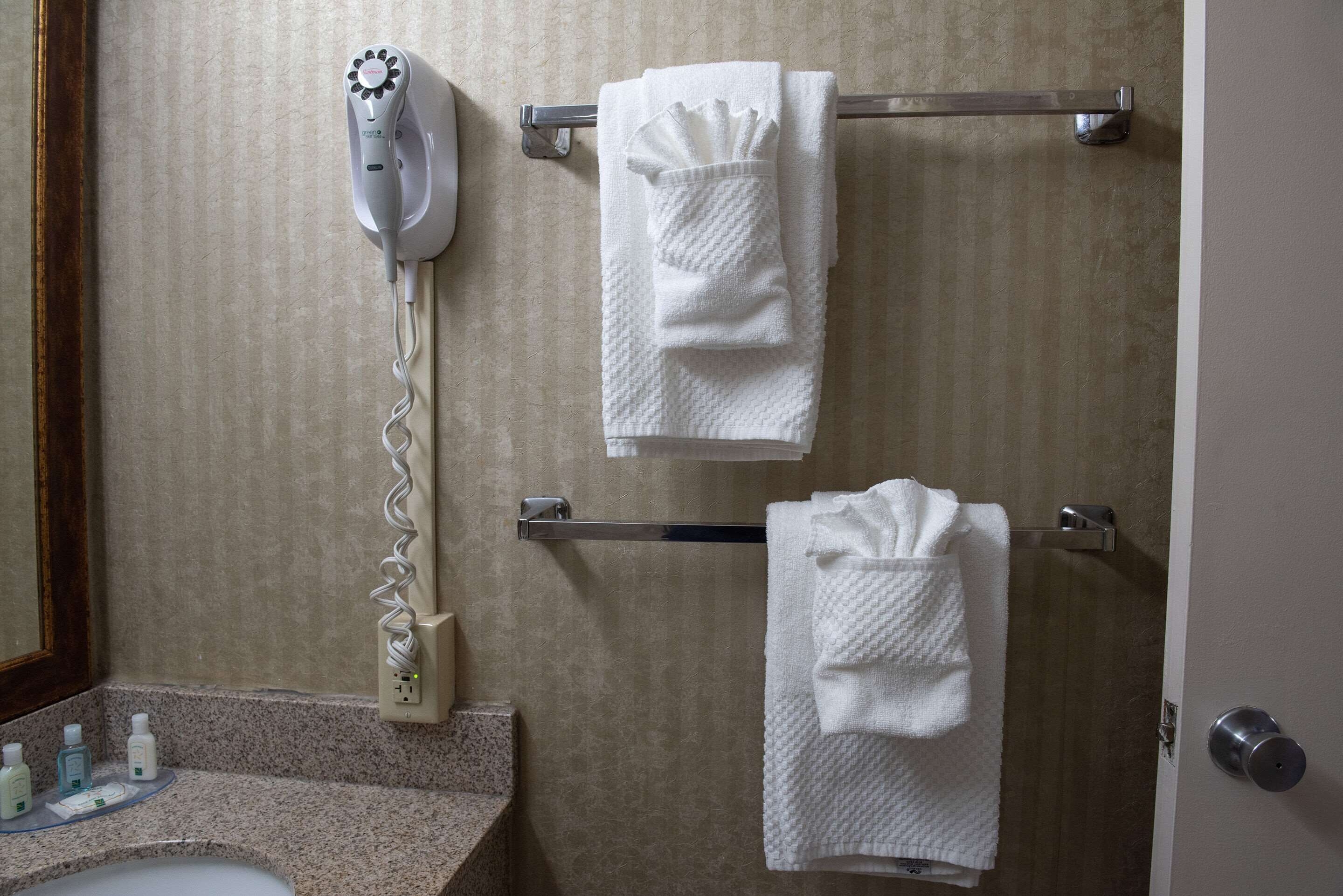 A bathroom with a towel rack holding three white towels, a hairdryer, and a mirror.