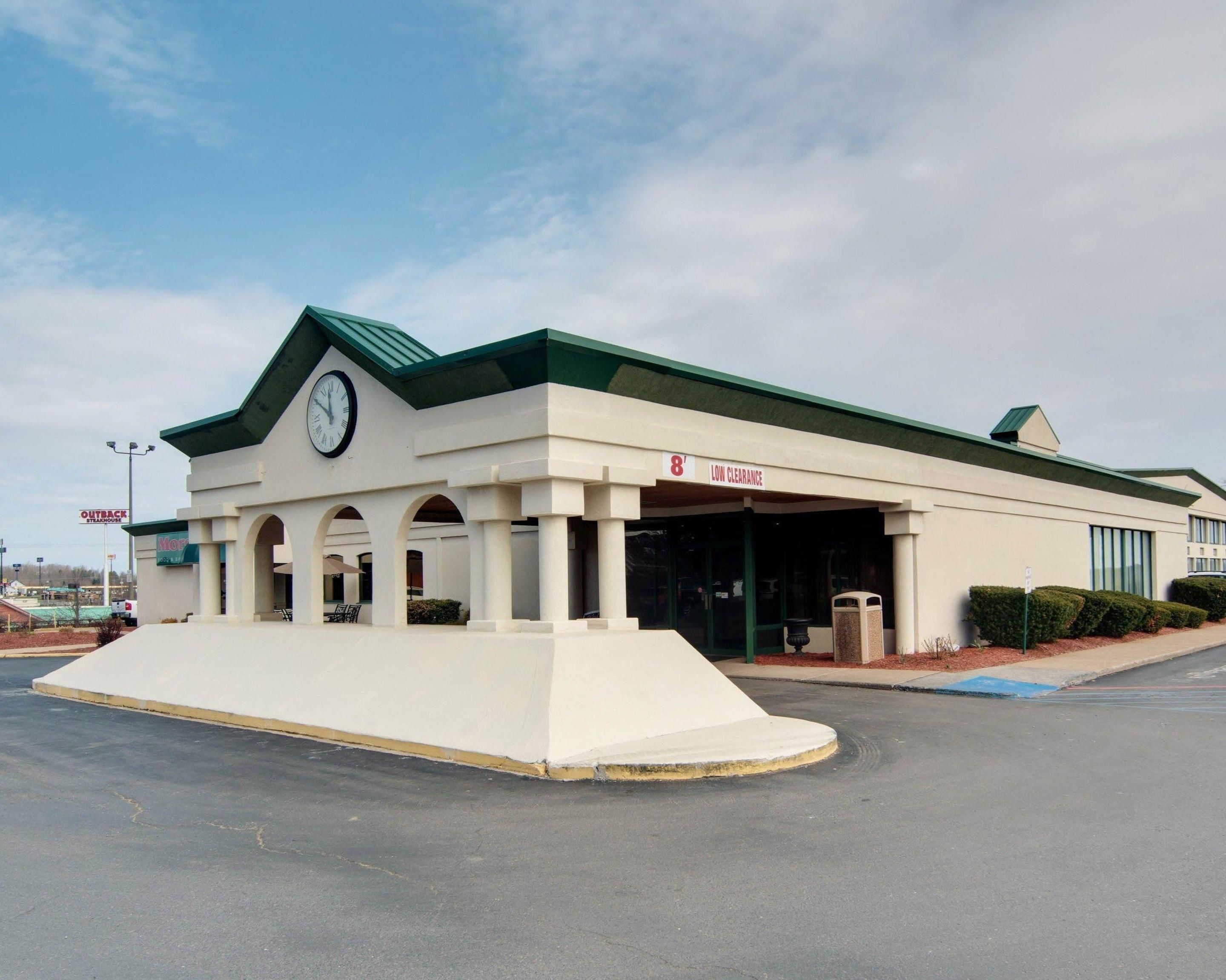 A building with a clock on the facade, a sign indicating 'LOW CLEARANCE', and a parking lot in front.