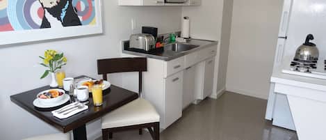 Une cuisine compacte équipée d’un four à micro-ondes, d’une cuisinière et d’un évier. On y trouve une table à manger avec des aliments pour le petit-déjeuner et une chaise.