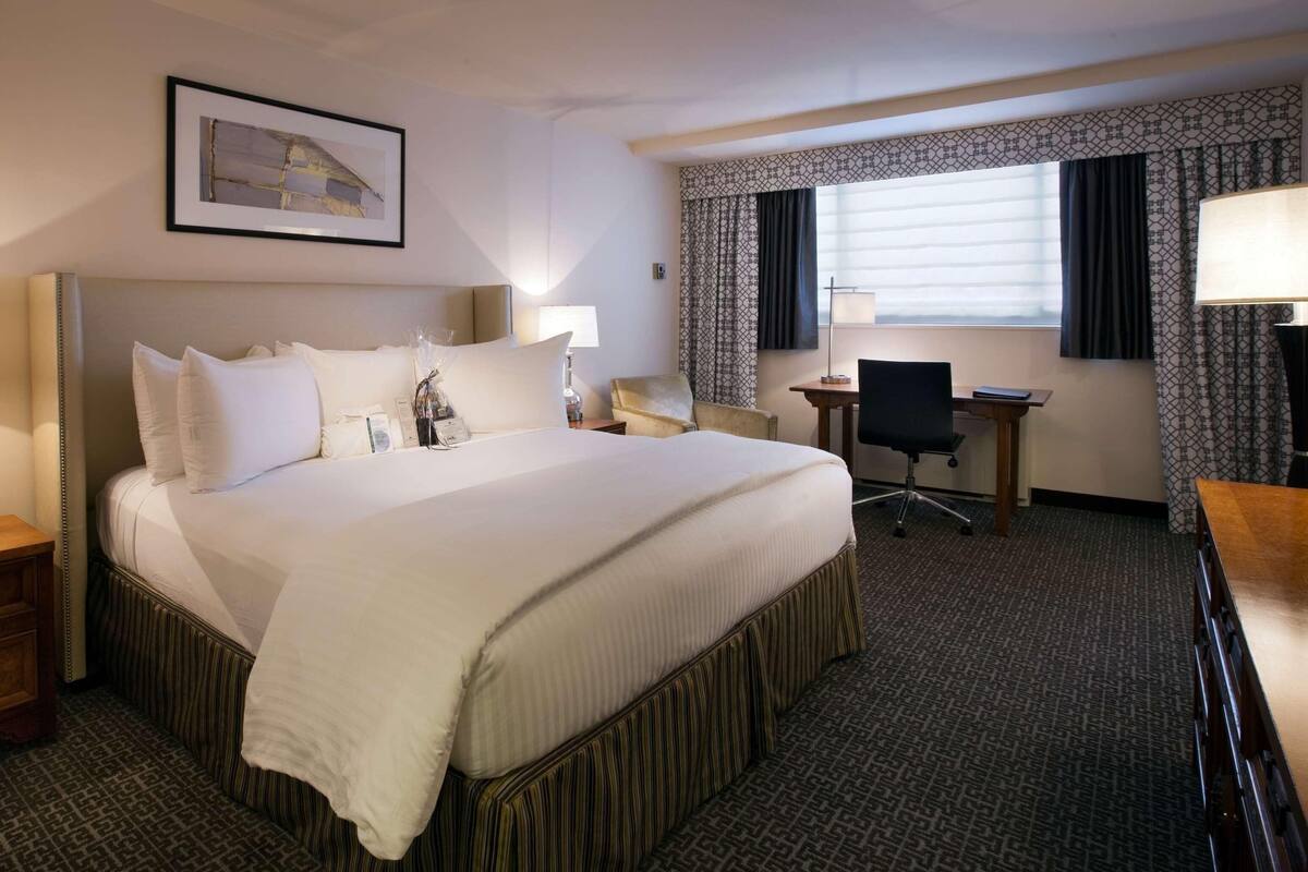 Quarto de hotel com uma cama grande, mesas de cabeceira, uma escrivaninha e uma cadeira.