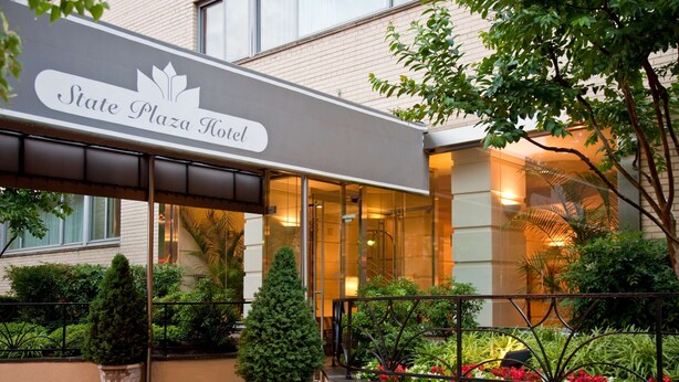 Fasaden på State Plaza Hotel är modern, med stora glasfönster och en välanlagd entré med planteringar och ett metallräcke.