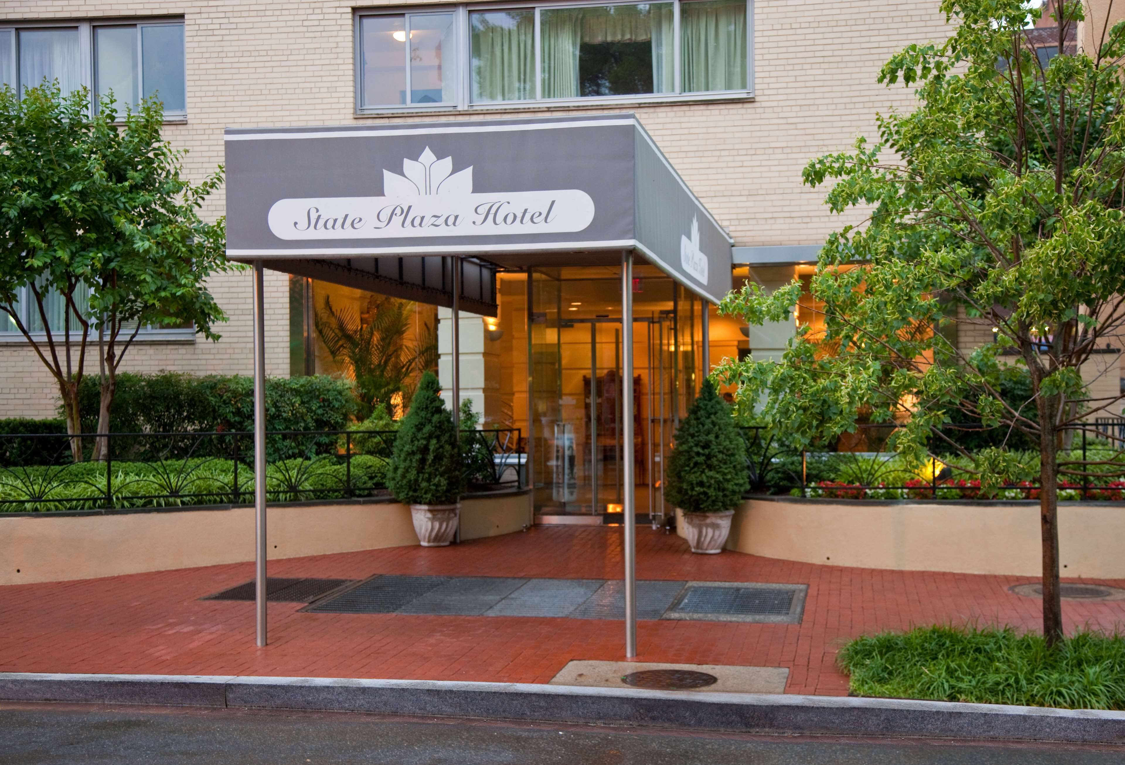 The entrance of the State Plaza Hotel with a covered walkway, potted plants, and a brick pathway.