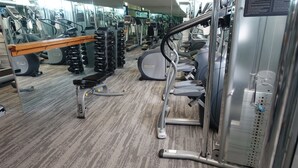 Un gimnasio con diversas máquinas de ejercicio, una banca y torres de pesas.