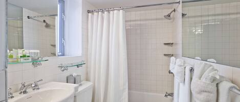 A modern bathroom with a white sink, toilet, and bathtub. There is a glass shelf above the sink and a shower curtain.