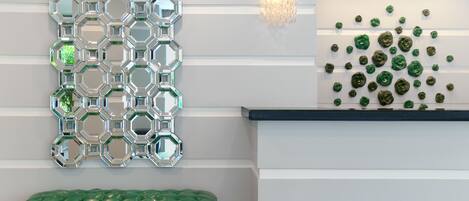 A reception area with a green bench, a wall-mounted hexagonal mirror pattern, a wall sconce, and a wall of green floral decorations.