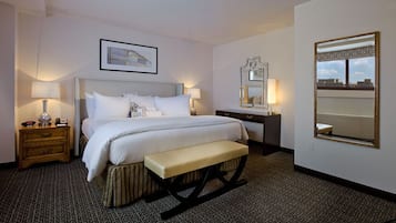 Ein Hotelzimmer mit einem großen Bett, Nachttischen, einer Bank, einem Spiegel und einem gerahmten Bild an der Wand.