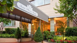 Exterior del Hotel State Plaza con un acceso cubierto, plantas en macetas y un jardín bien cuidado.