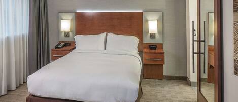 Habitación de hotel con una cama grande, una mesita de noche con lámpara, cabecero de madera y un espejo en la pared.