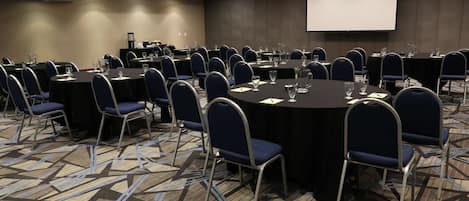 Un salón de conferencias con mesas redondas, sillas y una pantalla para proyector.