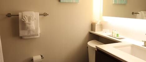 A bathroom with a toilet, a towel rack with a folded towel, a toilet paper holder, a sink with toiletries, and two wall-mounted paintings.