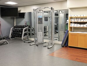 A gym with weightlifting equipment, a television, and a shelf with towels. - DoubleTree by Hilton Omaha Southwest (Omaha)