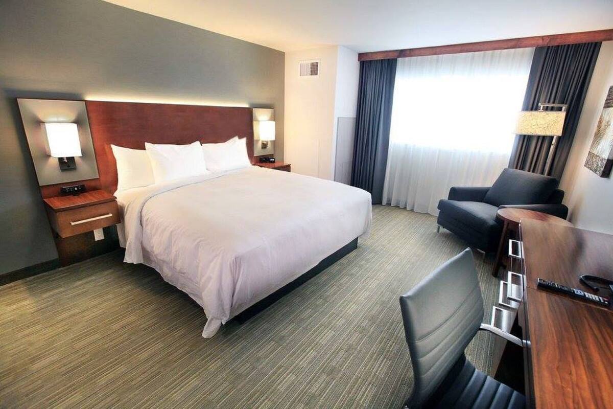 Een hotelkamer met een groot bed, een bureau met stoel, een lamp en een raam met gordijnen.
