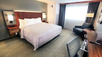 A hotel room with a large bed, a desk with a chair, a lamp, and a window with curtains.