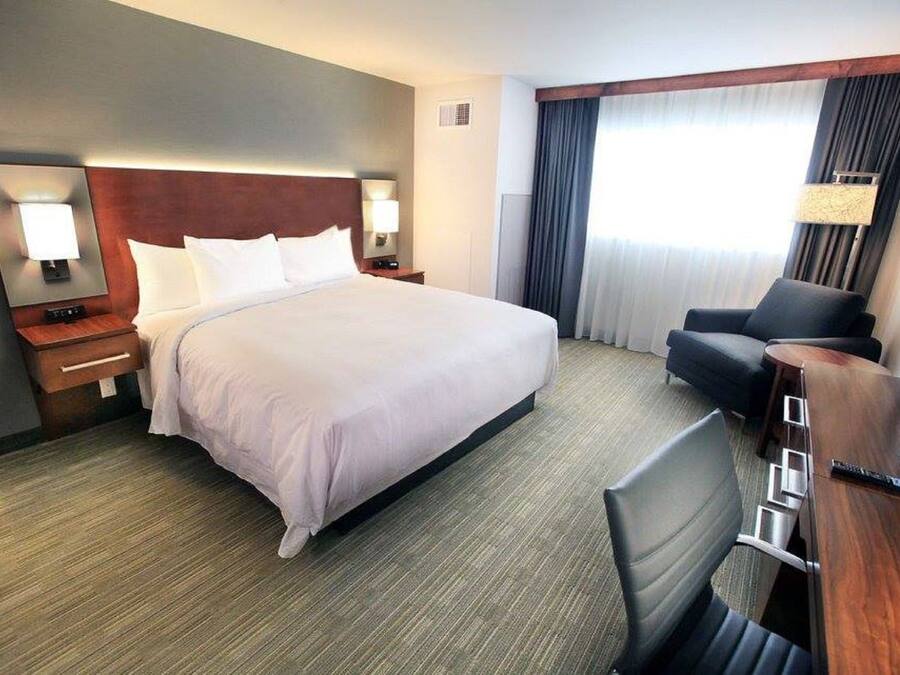 A hotel room with a large bed, a desk with a chair, a lamp, and a window with curtains.