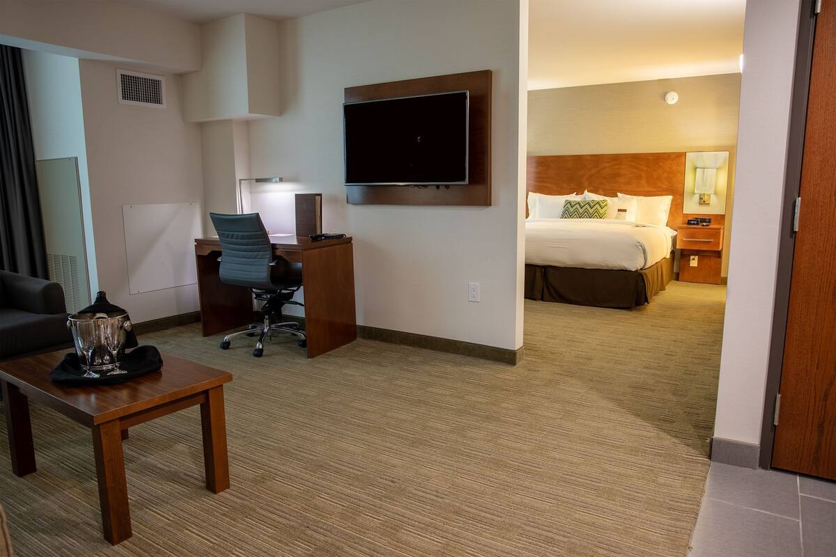 Hotelkamer met een bed, een bureau met stoel, een aan de muur bevestigde televisie en een kleine tafel met een karaf.